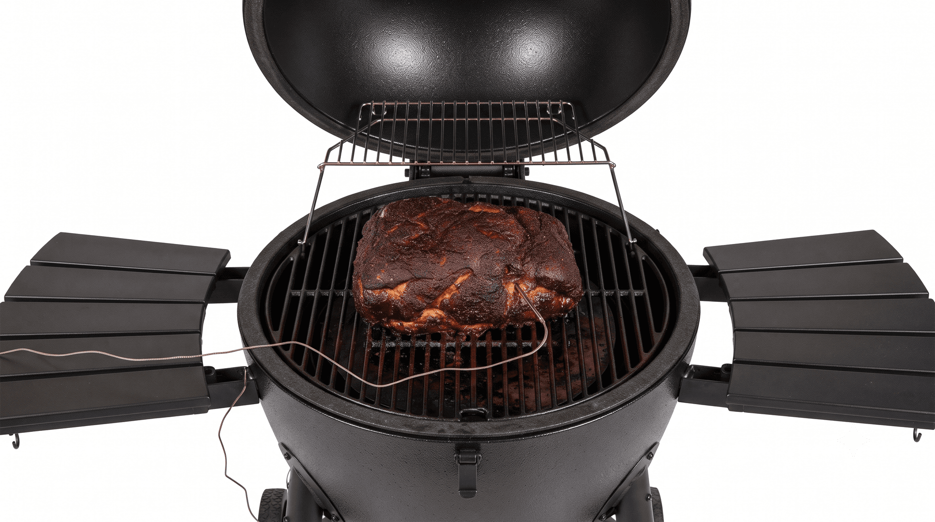 Pork shoulder with dark bark on a cast iron grate inside a graphite steel kamado with a probe wire