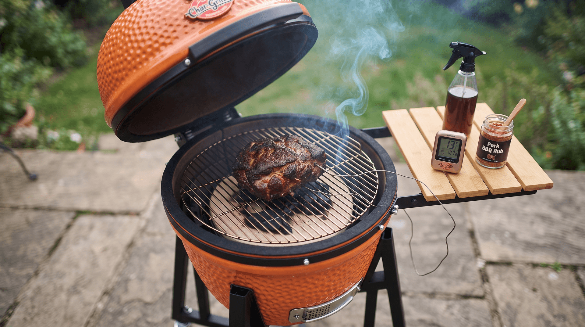 Small pork shoulder on the grate of a compact ceramic kamado with a probe display on the side shelf