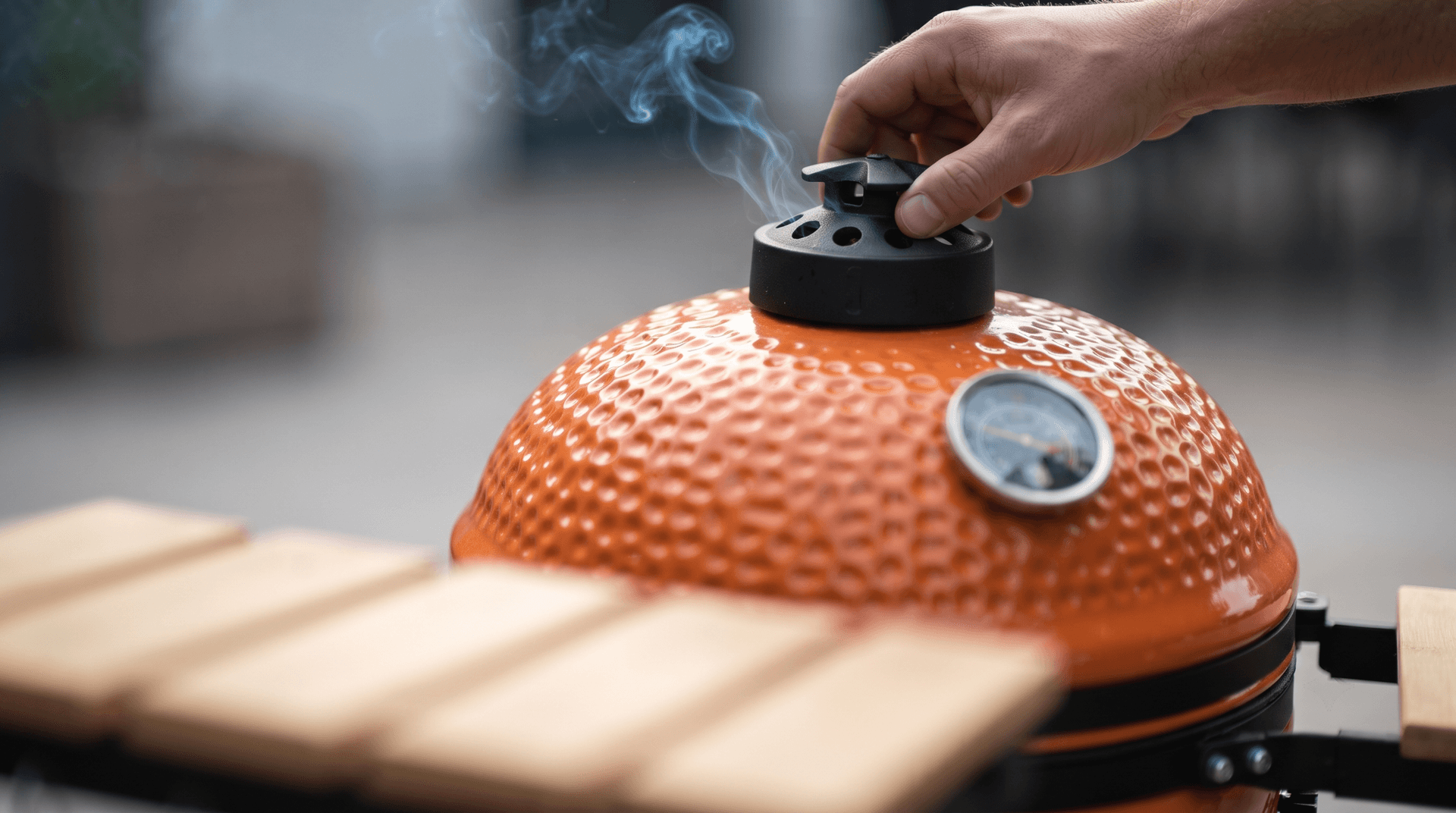 Hand turning the cast iron top vent on a small ceramic kamado dome with smoke rising