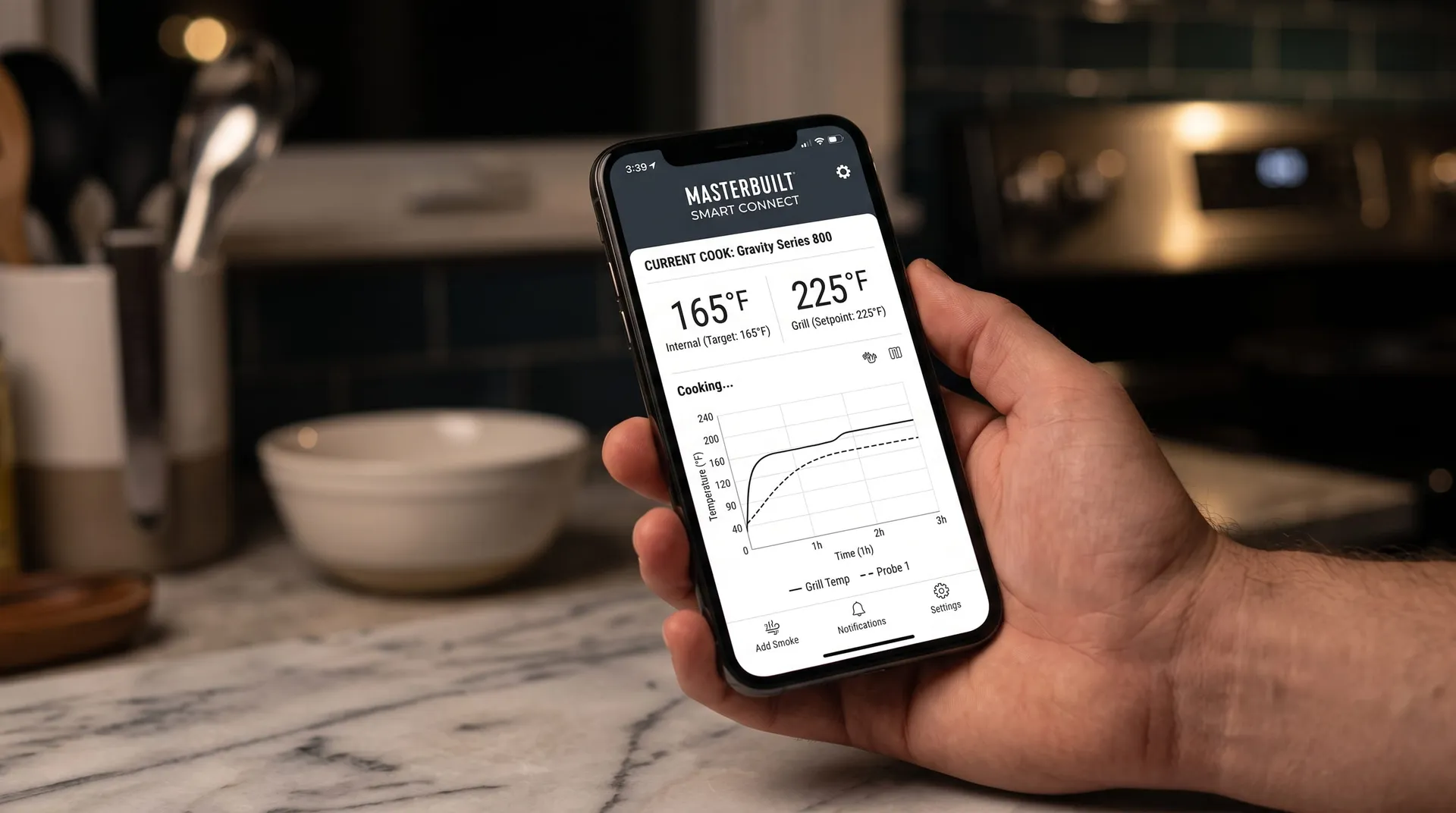 Hand holding a phone showing the Masterbuilt app with probe and grill temperatures and a cook graph