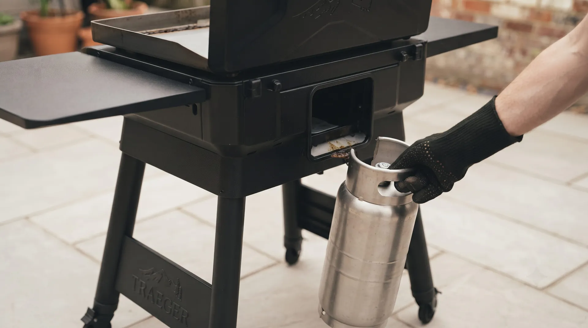 Gloved hand pulling the grease keg out from the back of a Traeger Flatrock griddle